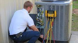 A technician kneels beside an outdoor air conditioning unit, using diagnostic equipment to check its functionality.